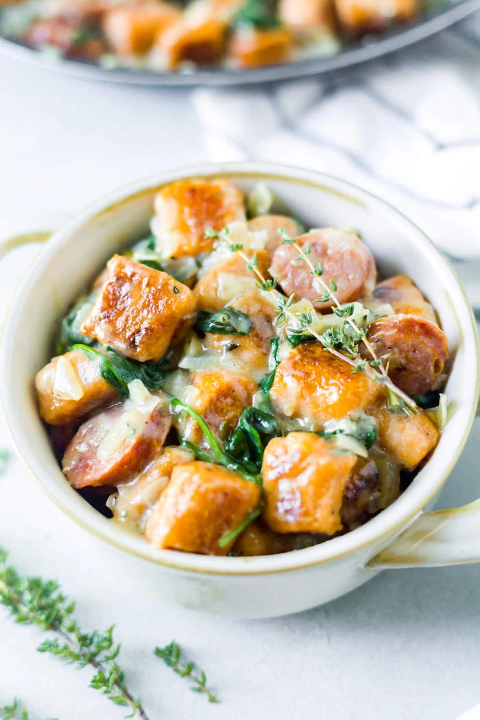 small white bowl filled with baked gnocchi in cheesy sauce with spinach what is gnocchi placed on white surface
