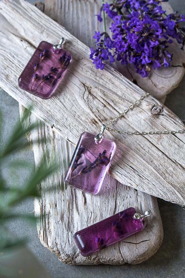 three necklace pendants made with pink resin and dried lavender making resin jewelry arrranged on wooden blocks