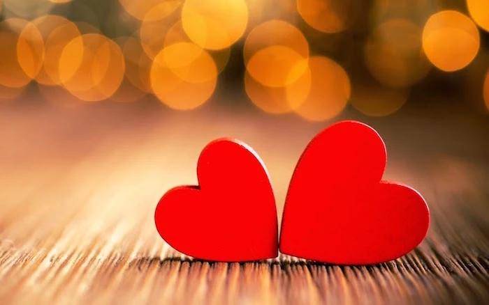 two red hearts placed next to each other placed on wooden surface valentines background blurred lights in the background
