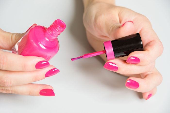valentine nail designs female hands with medium length squoval nails covered with pink nail polish holding the bottle
