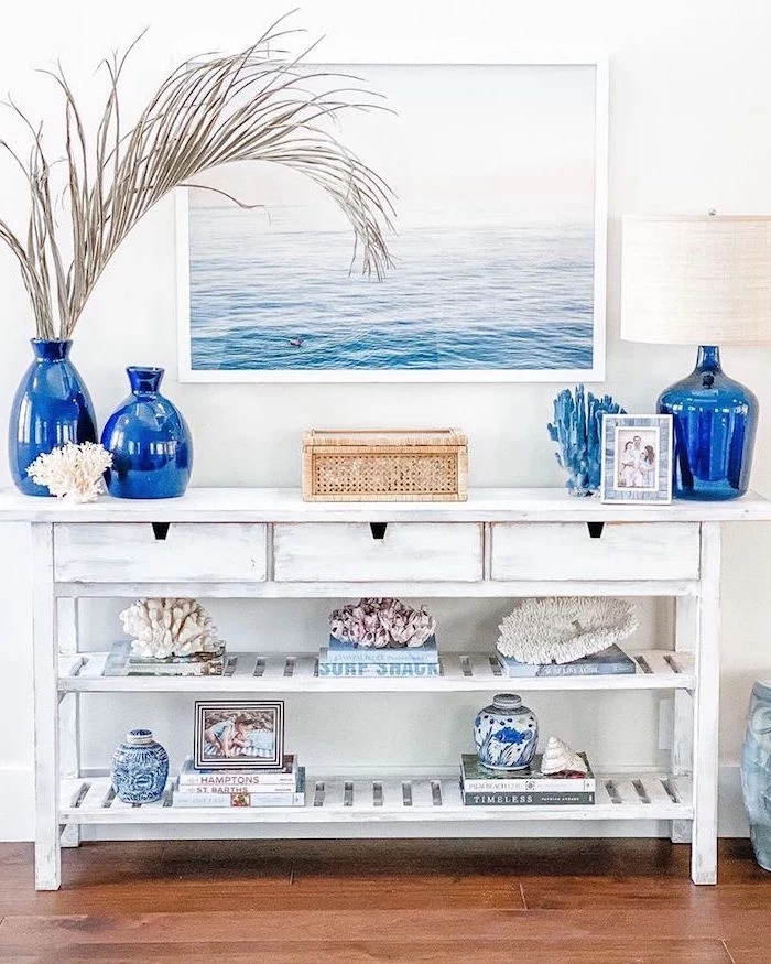 white wooden table with blue vases books and corals on it coastal living room framed ocean painting above it