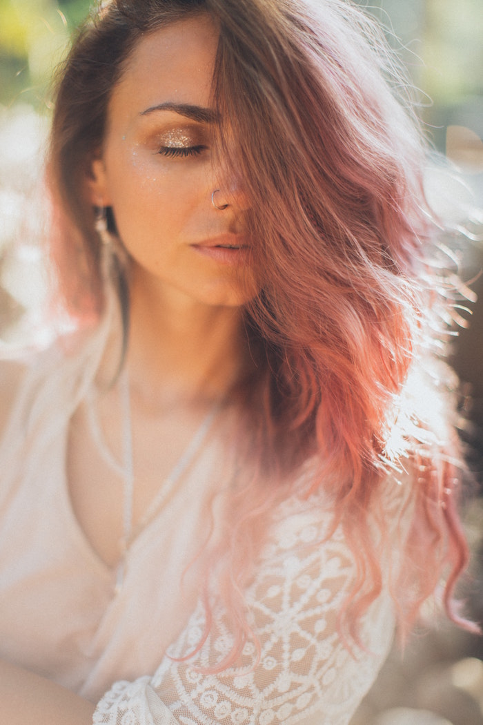 woman with medium length wavy hair in pink color keep your hair healthy wearing white lacy top glitter eyeshadow