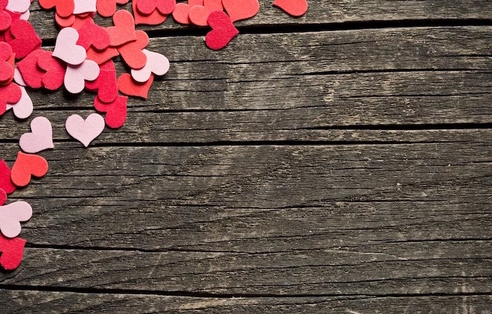 wooden background when is valentines day lots of small hearts in one of the corners in different shades of pink and red