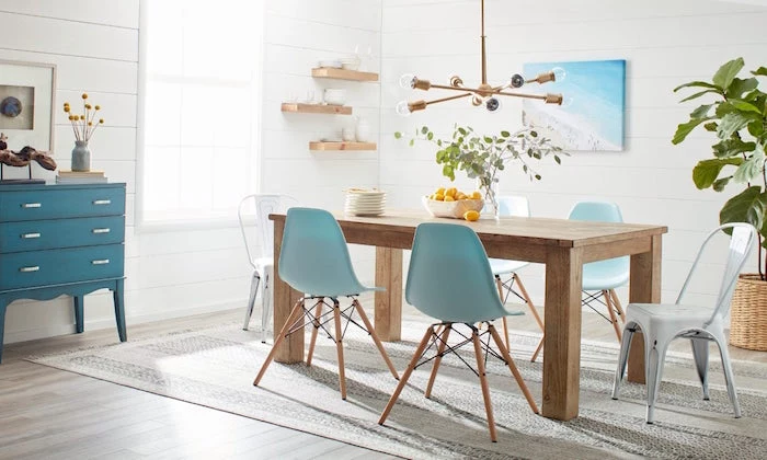wooden dining table blue and white chairs around it on gray carpet on wooden floor coastal decorating ideas white shiplap walls
