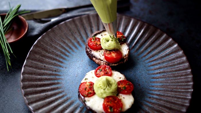 avocado mixture added to stuffed mushrooms with piping bag easy appetizers finger foods placed on ceramic plate