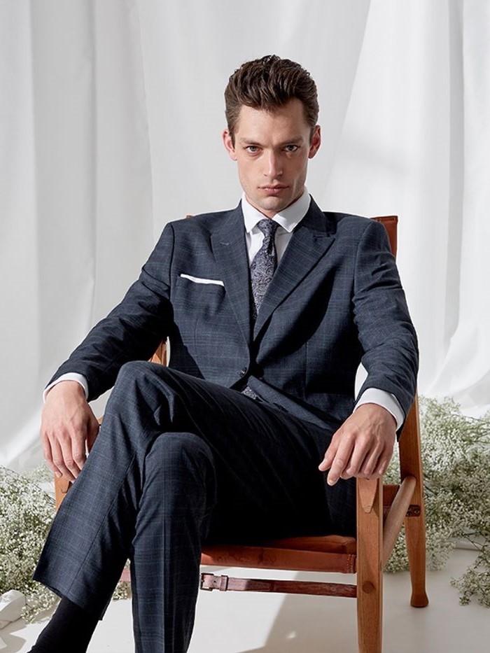brunette man sitting in brown leather chair fabrics for suits wearing navy blue suit with white shirt and floral tie