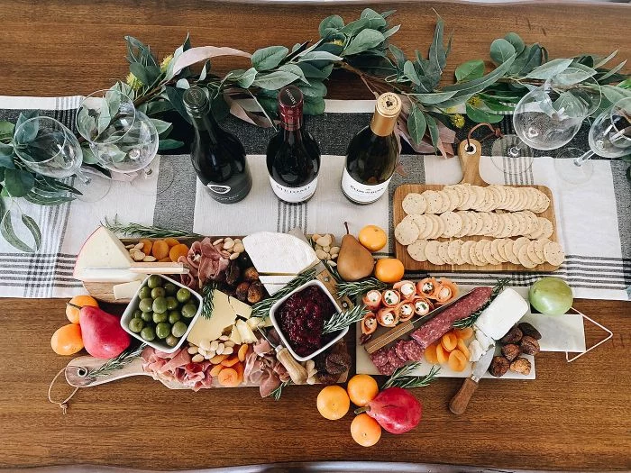 charcuterie board with meat cheese fruits crackers three wine bottles and wine glasses next to it
