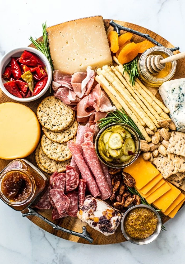 charcuterie platter with different types of meat cheese crackers veggies on round wooden tray