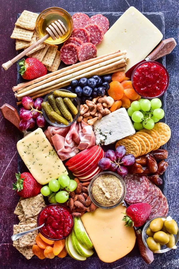 cheeses crackers meats pickles condiments fruits arranged on black stone board charcuterie platter