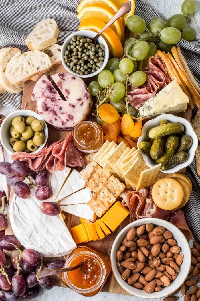 cheeses meats bread crackers grapes pickles olives nuts arranged on wooden board cheese board ideas