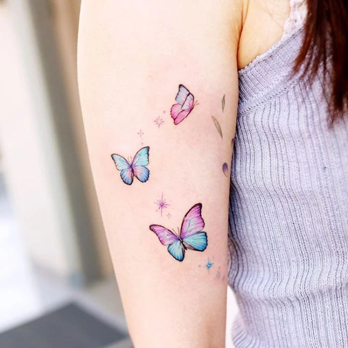 colored butterflies in purple and blue stars around them butterfly tattoo on arm three butterflies arm tattoo