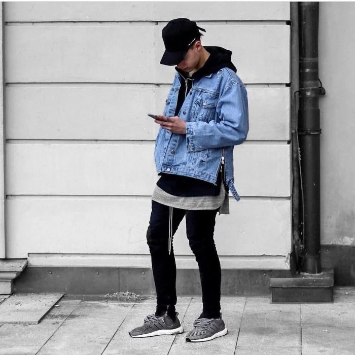denim jacket paired with black jeans and hoodie gray sneakers streetwear clothing man standing on sidewalk