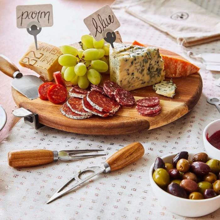 different types of cheese meat grapes on small round wooden board how to make a charcuterie board cheese knives next to it