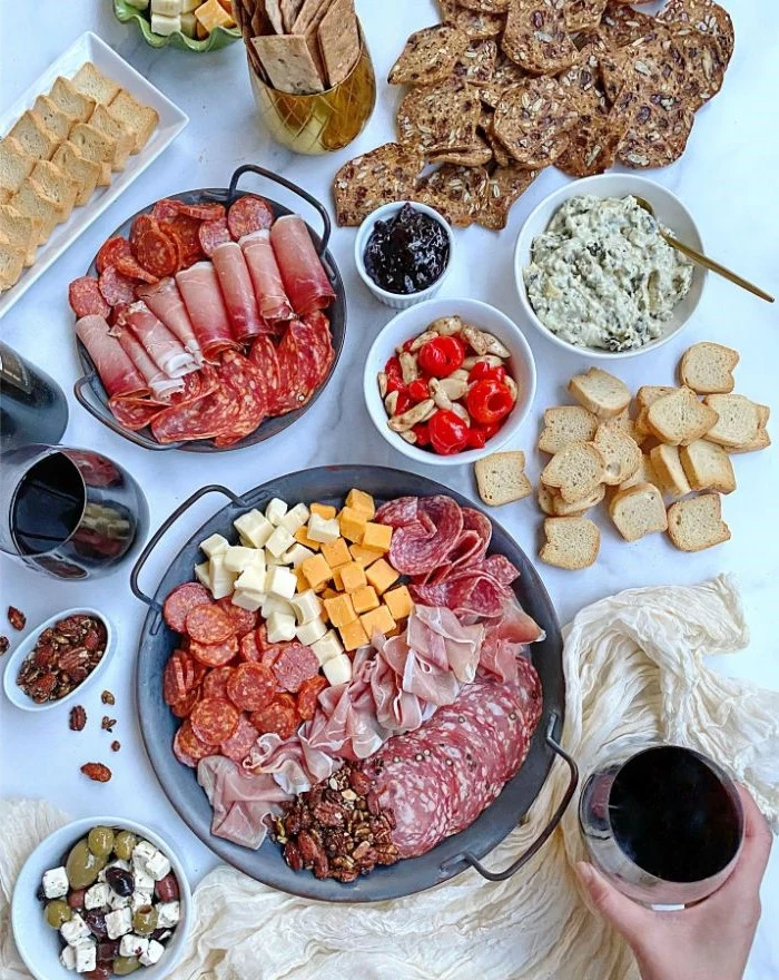 different types of meat and cheese arranges on two round trays charcuterie board ideas condiments and bread on the side