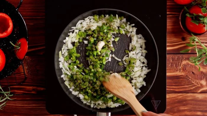 finger food appetizers chopped onion and peppers cooking in a saucepan with wooden spatula