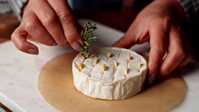finger foods for party brie cheese sliced in the middle with garlic and rosemary placed in between the slits