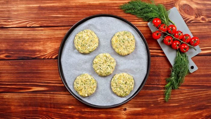 five zucchini fritters party snack ideas placed on paper lined baking tray placed on wooden surface