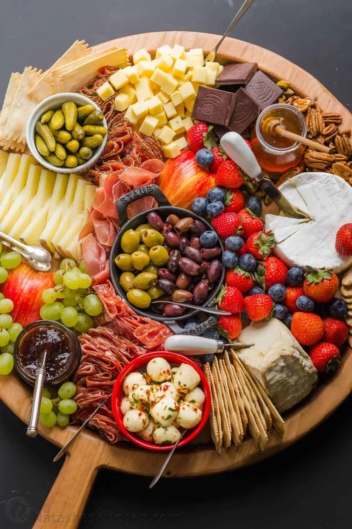 fruits cheeses meats condiments olives pickles charcuterie platter arranged on round wooden board
