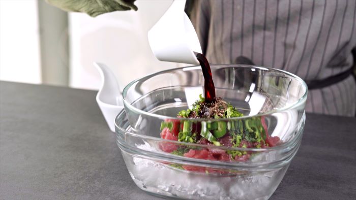 glass bowl placed on top of another glass bowl filled with ice appetizers for a crowd tuna tartare mixture