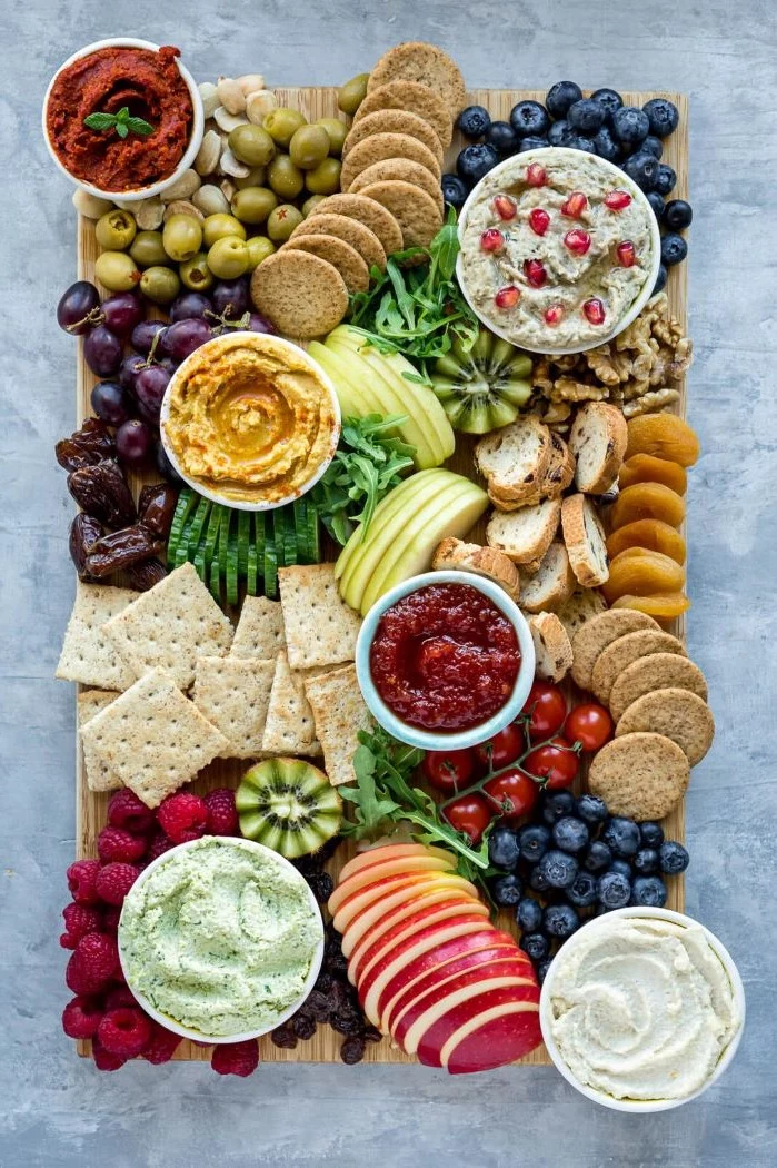 hummus olives veggies fruits crackers arranged on wooden tray what is charcuterie with condiments in bowls