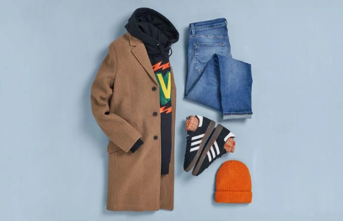 jeans black sneakers and hoodie beige coat orange beanie streetwear fashion blue background