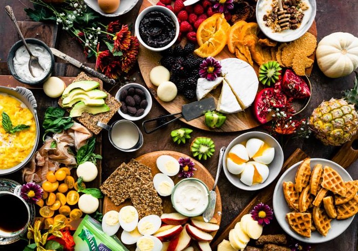 large wooden table covered with wooden boards meat and cheese board with crackers different types of fruits