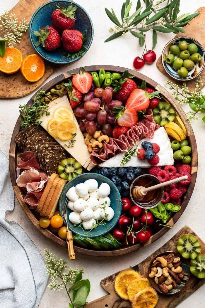 meat and cheese platter round wooden board covered with cheeses meats fruits veggies condiments