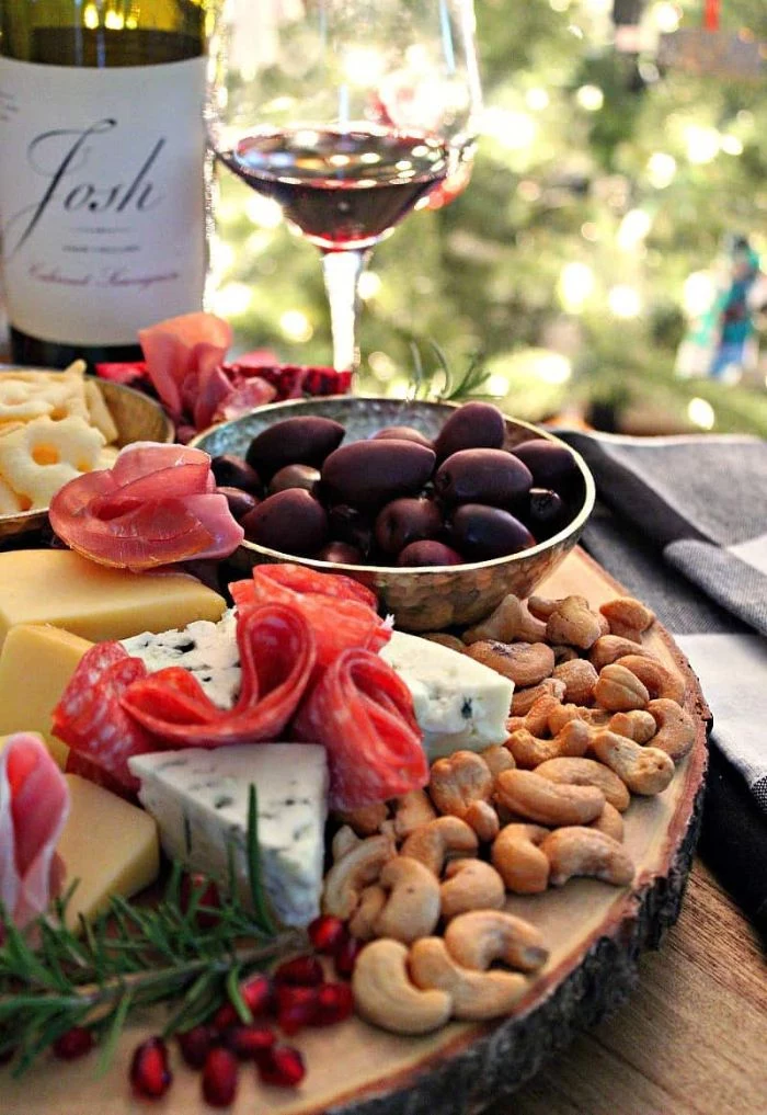 olives in a bowl meat and cheese board with nuts rosemary wine glass on the side