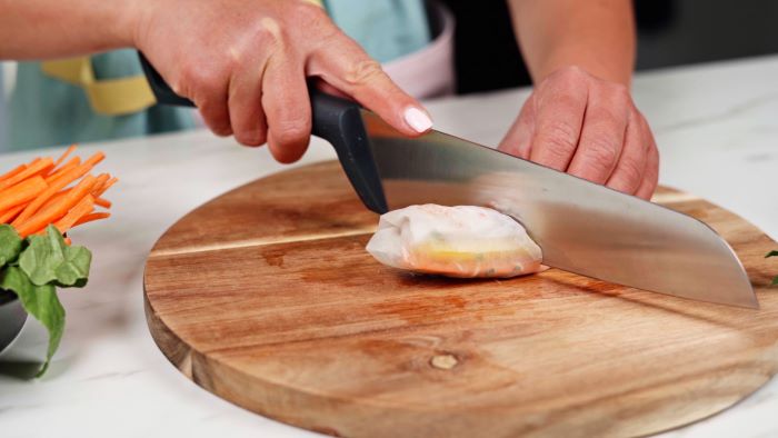 party snack ideas spring rolls rolled up being cut in half with large knife on wooden cutting board