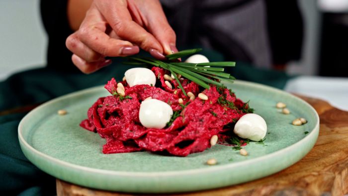 plate with pasta with beetroot sauce how to make homemade pasta being garnished with baby mozzarella pine nuts wild onion