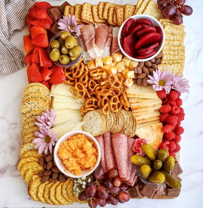 pretzels crackers cheeses fruits pickles charcuterie platter chocolates purple flowers for decoration