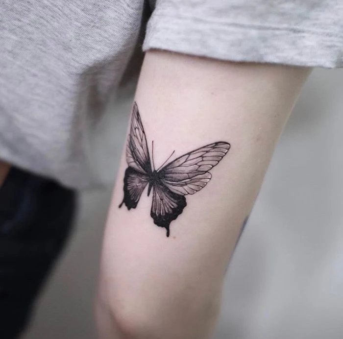 small butterfly tattoo on the back of the arm above the elbow in black and white