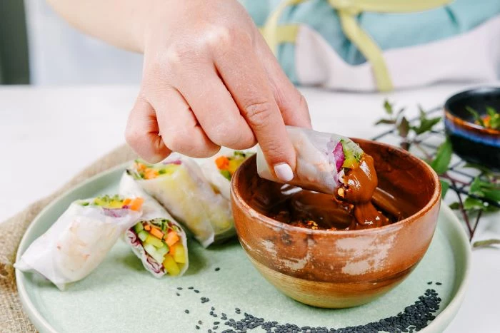spring roll being dipped in sauce in wooden bowl easy appetizers for a crowd on ceramic plate
