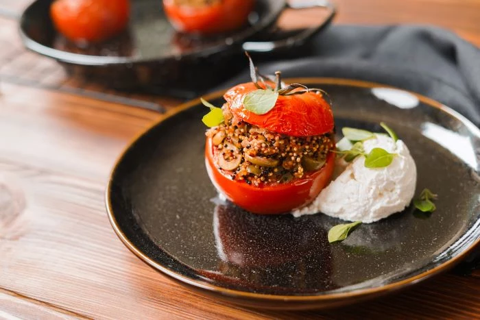 stuffed tomato with quinoa mixture appetizers for a crowd placed with ricotta cheese on black ceramic plate