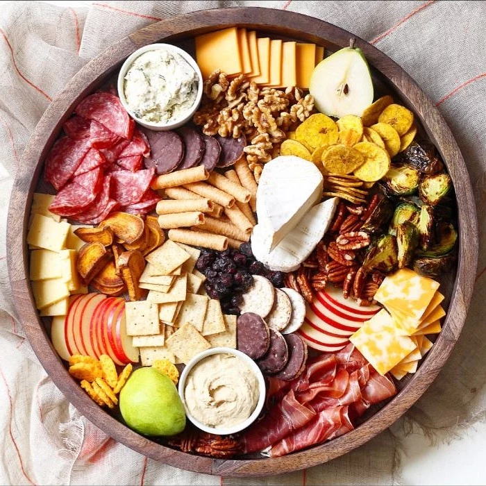 what is charcuterie round wooden tray filled with meats cheeses crackers nuts condiments in small bowls