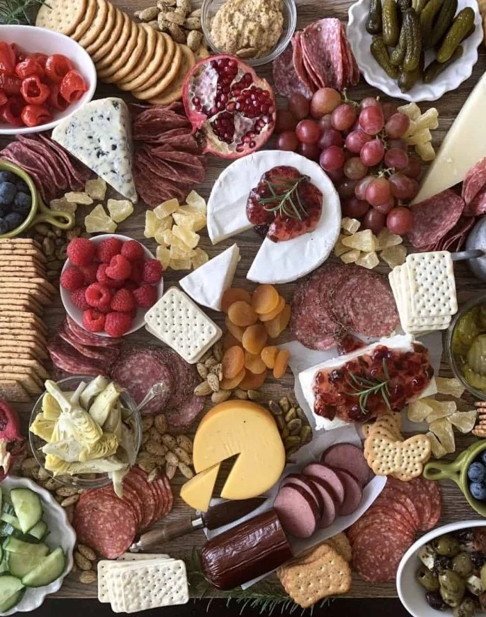 wooden board covered with fruits crackers meat and cheese platter condiments veggies