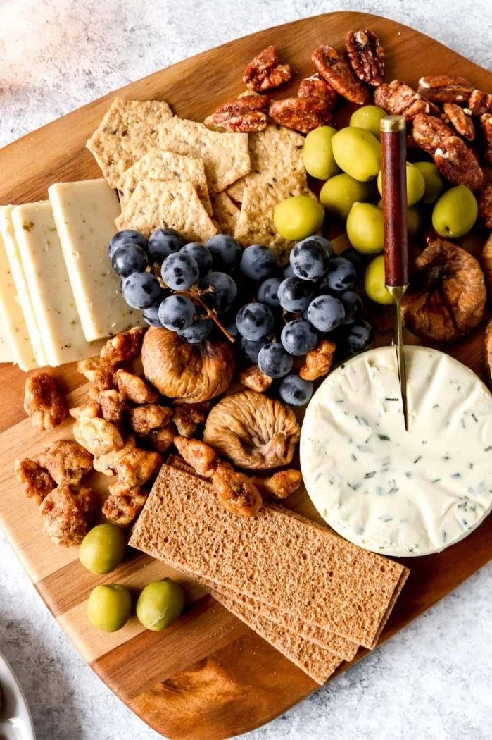 wooden board with cheeses crackers grapes dried fruit olives meat and cheese platter