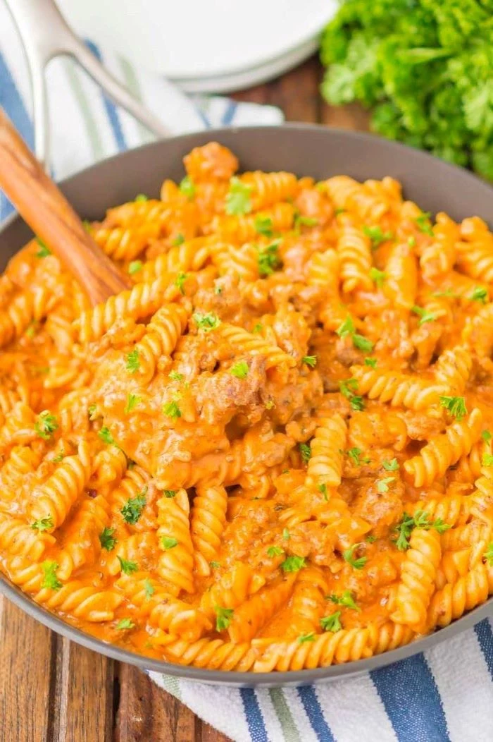 wooden spoon in saucepan best pasta dishes creamy ground beef pasta garnished with parsley