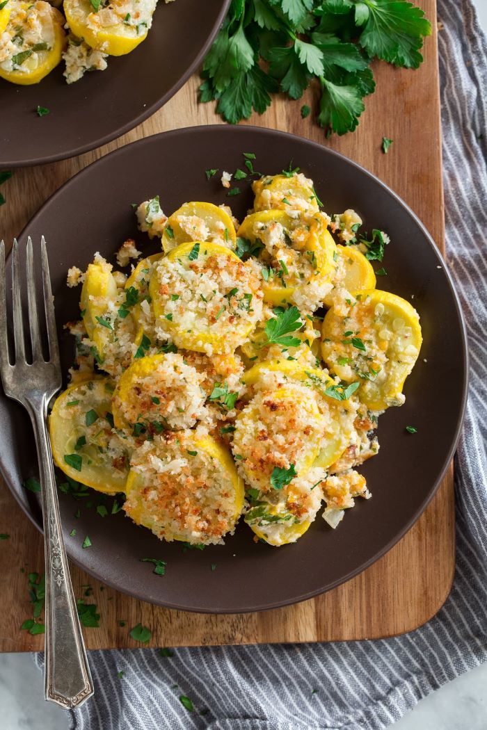 black plate with yellow squash casserole garnished with shredded cheese breadcrumbs and parsley