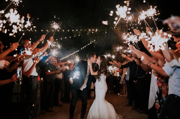 bride and groom kissing backyard wedding decorations people standing around them holding sparklers
