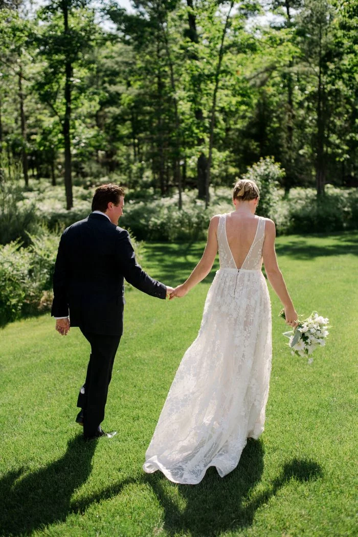 bride and groom walking on green grass field home wedding ideas lots of trees in the background