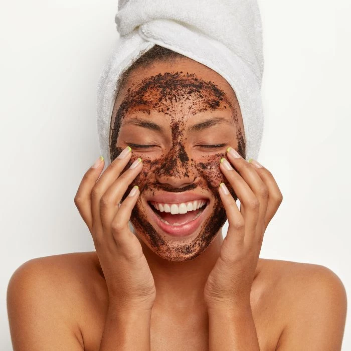 coffee grinds mask on womans face with white towel on her head homemade face mask white background