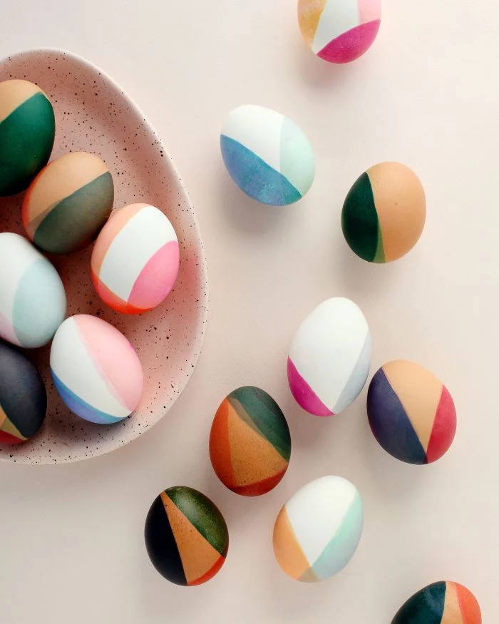 color blocked eggs in different colors easter egg coloring scattered around egg shaped plate on white surface
