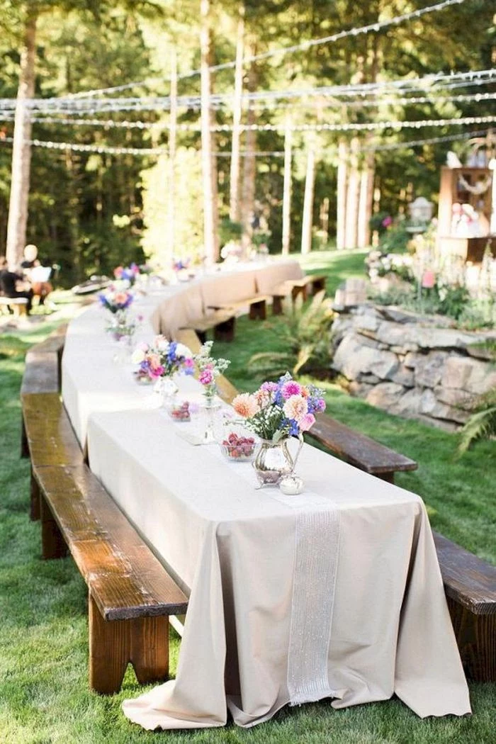colorful flower bouquets on long table with white cloth on it backyard wedding decorations vintage benches around it