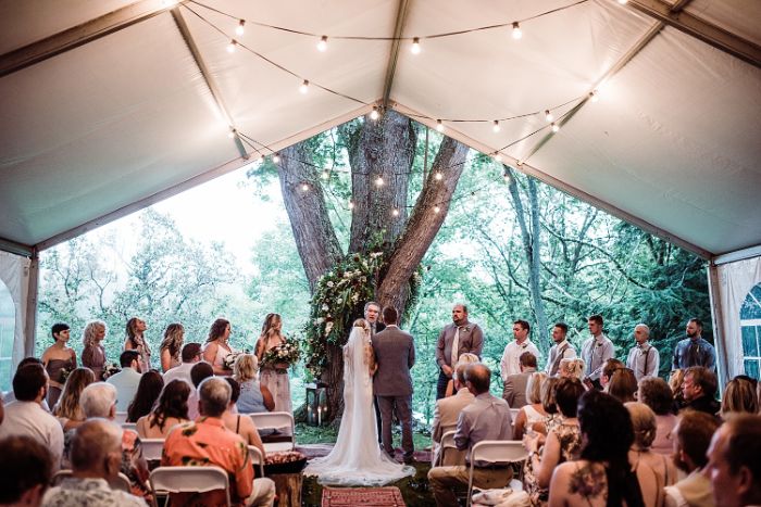 diy wedding ideas bride and groom standing in front of large tree tent set up in front of it