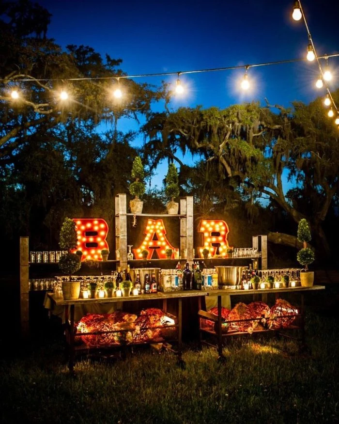drinks bar outside with wood tables sign with lights backyard wedding strings of lights hanging above