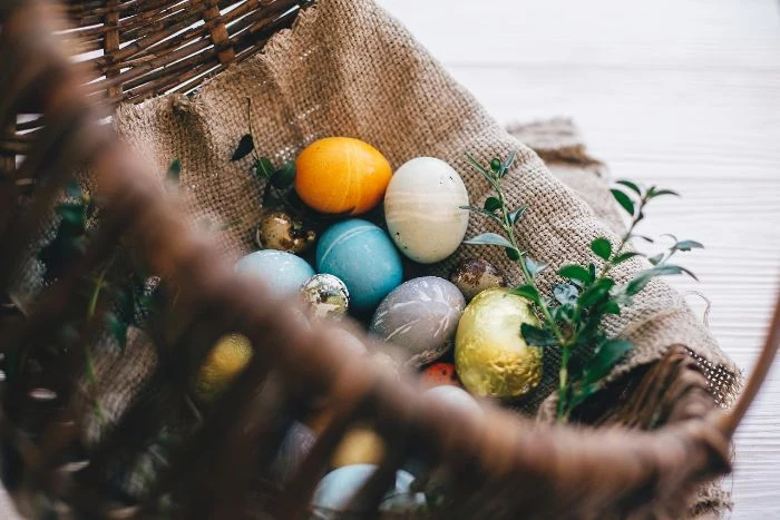 dying eggs with food coloring eggs in yellow blue gray and gold inside wooden basket with burlap cloth
