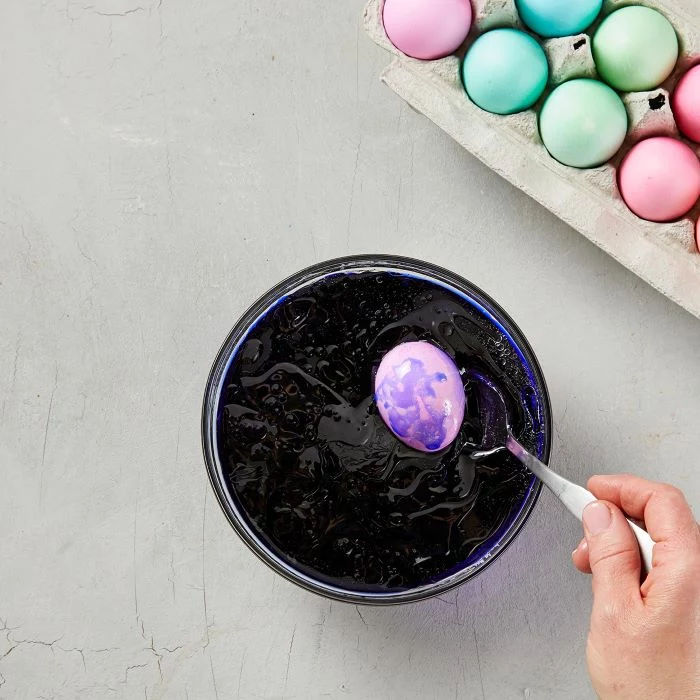 egg being dipped in bowl filled with dye and oil how to dye eggs with food coloring stirred with a spoon