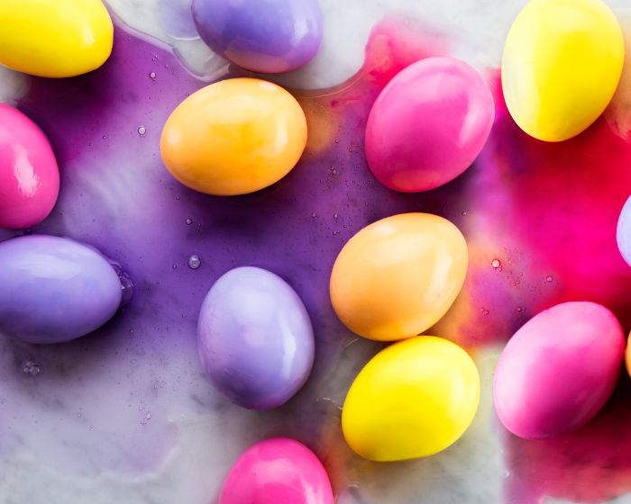 eggs colored in yellow purple pink easter egg designs scattered around surface with colorful liquid on it