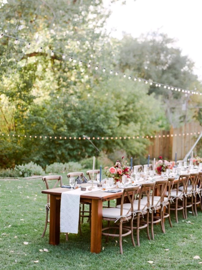 flower bouquets on wood table with lots of chairs strings of lights hanging above it rustic wedding ideas placed on green grass field
